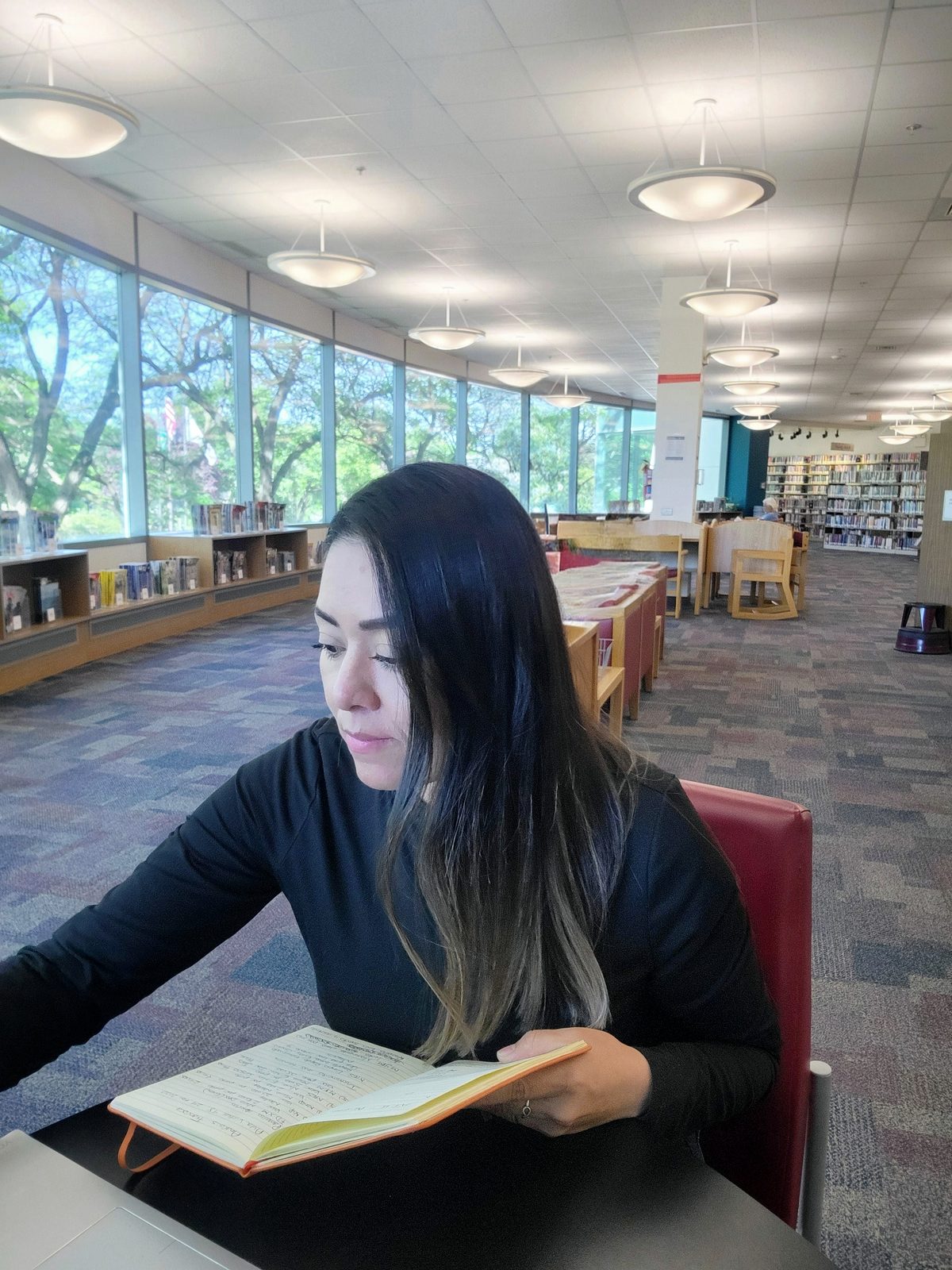 Marisol investigando en la biblioteca, libreta en mano